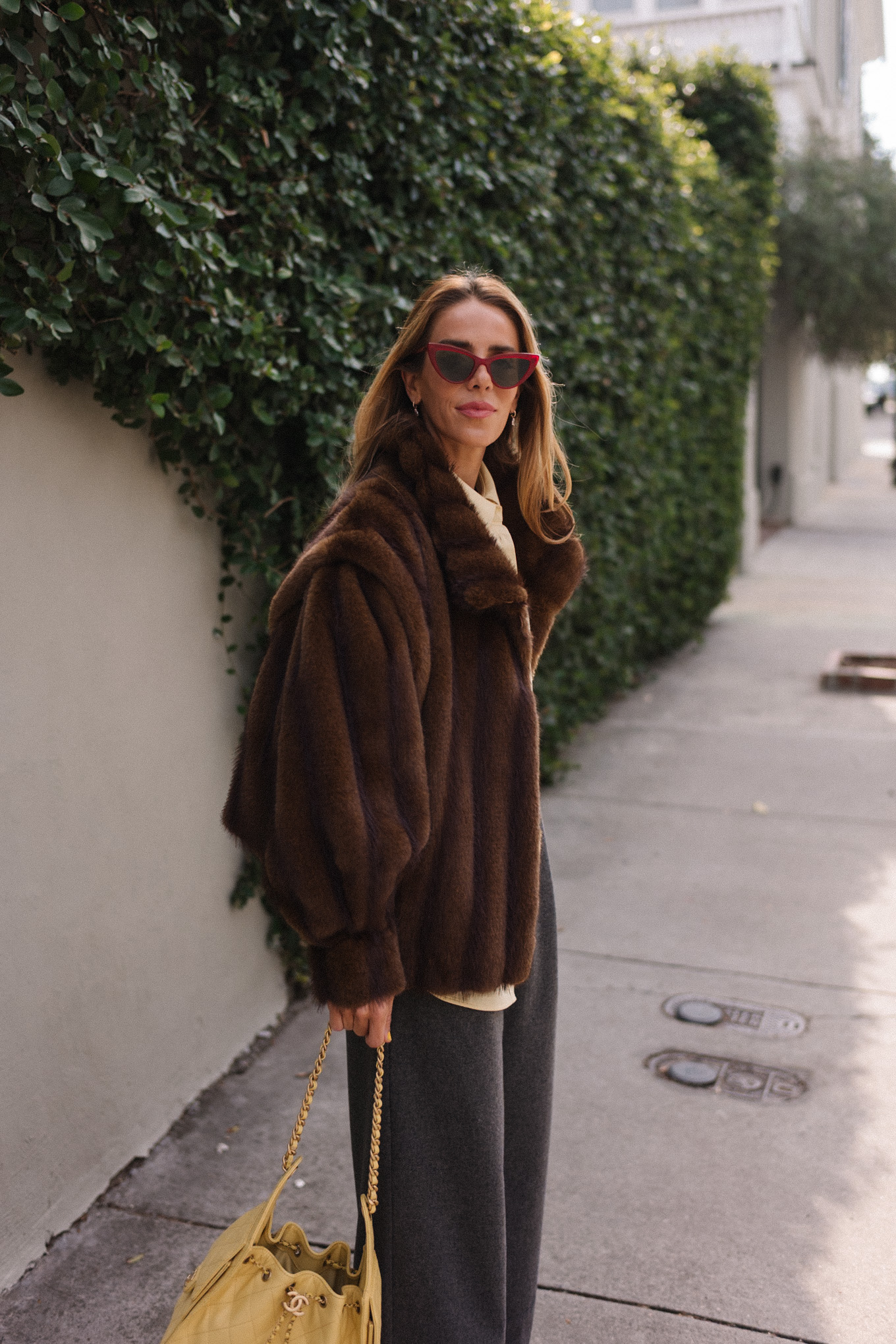 brown faux fur coat yellow button down shirt grey pants yellow tote red flats