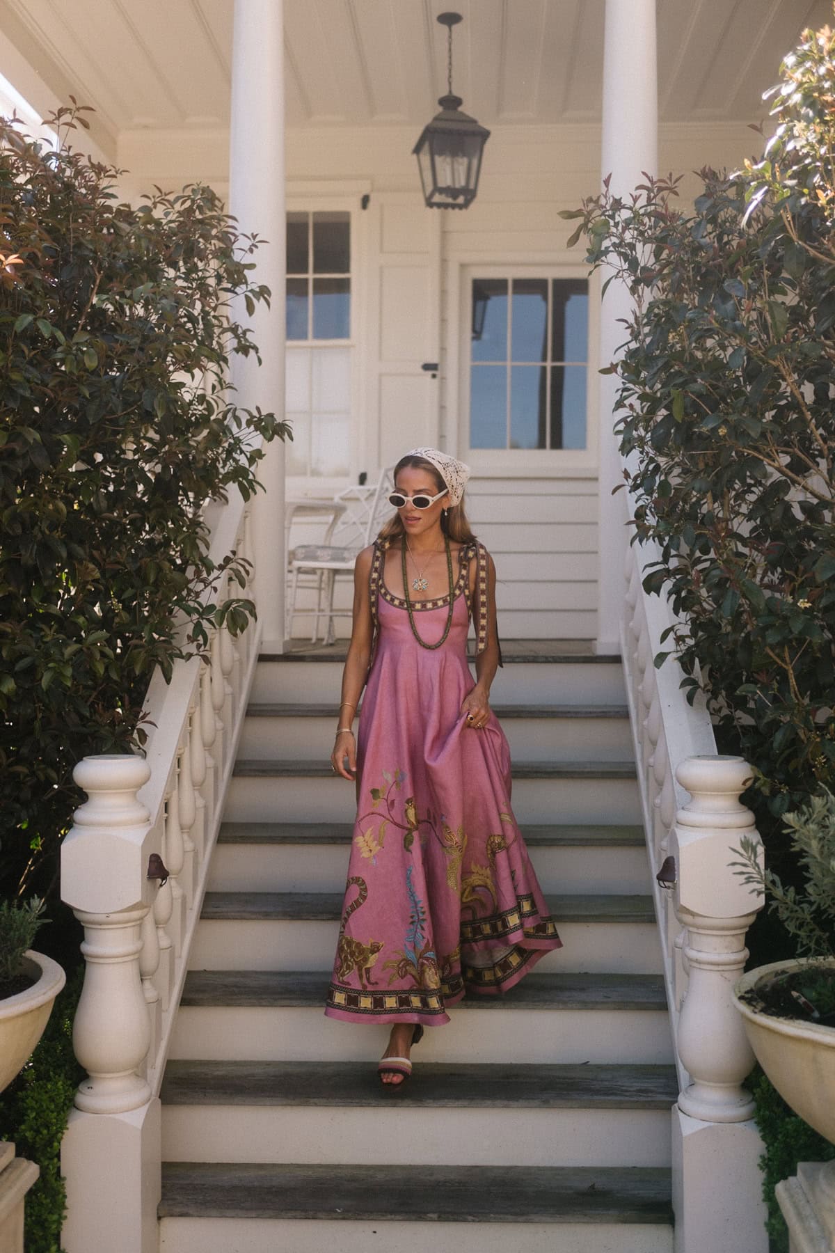 Woman in pink boho maxi dress with sunglasses on porch stairs.